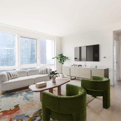 Modern living room at The Bold LIC apartments with large windows, a gray sofa, green chairs, and a colorful rug.